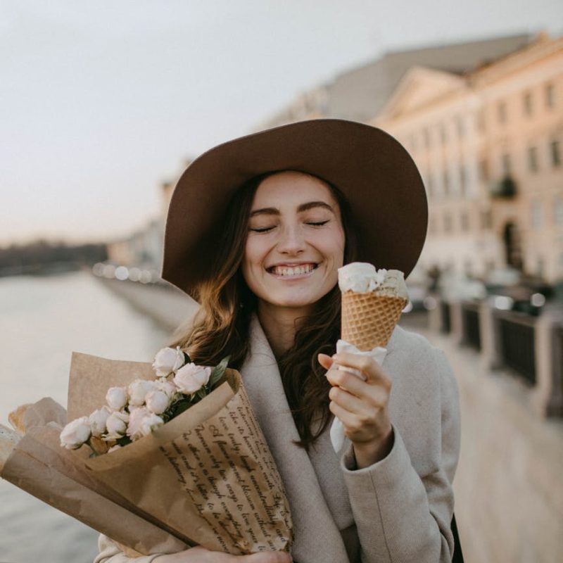 woman wearing brown coat holding white flower bouquet and ice cream