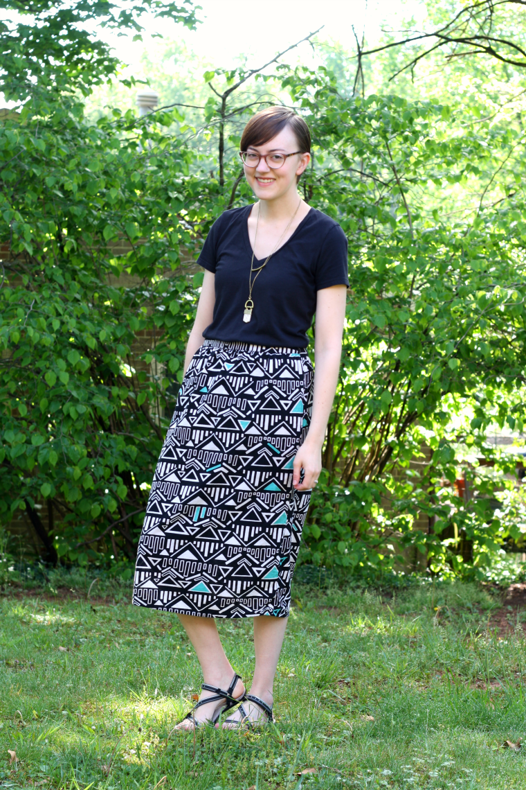 Leah stands in verdant green backyard wearing a black shirt and triangle print skirt - Mata Traders Outfit and Review