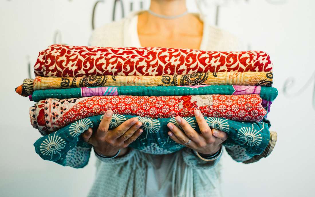 woman holds stack of kantha quilts - A History of Kantha