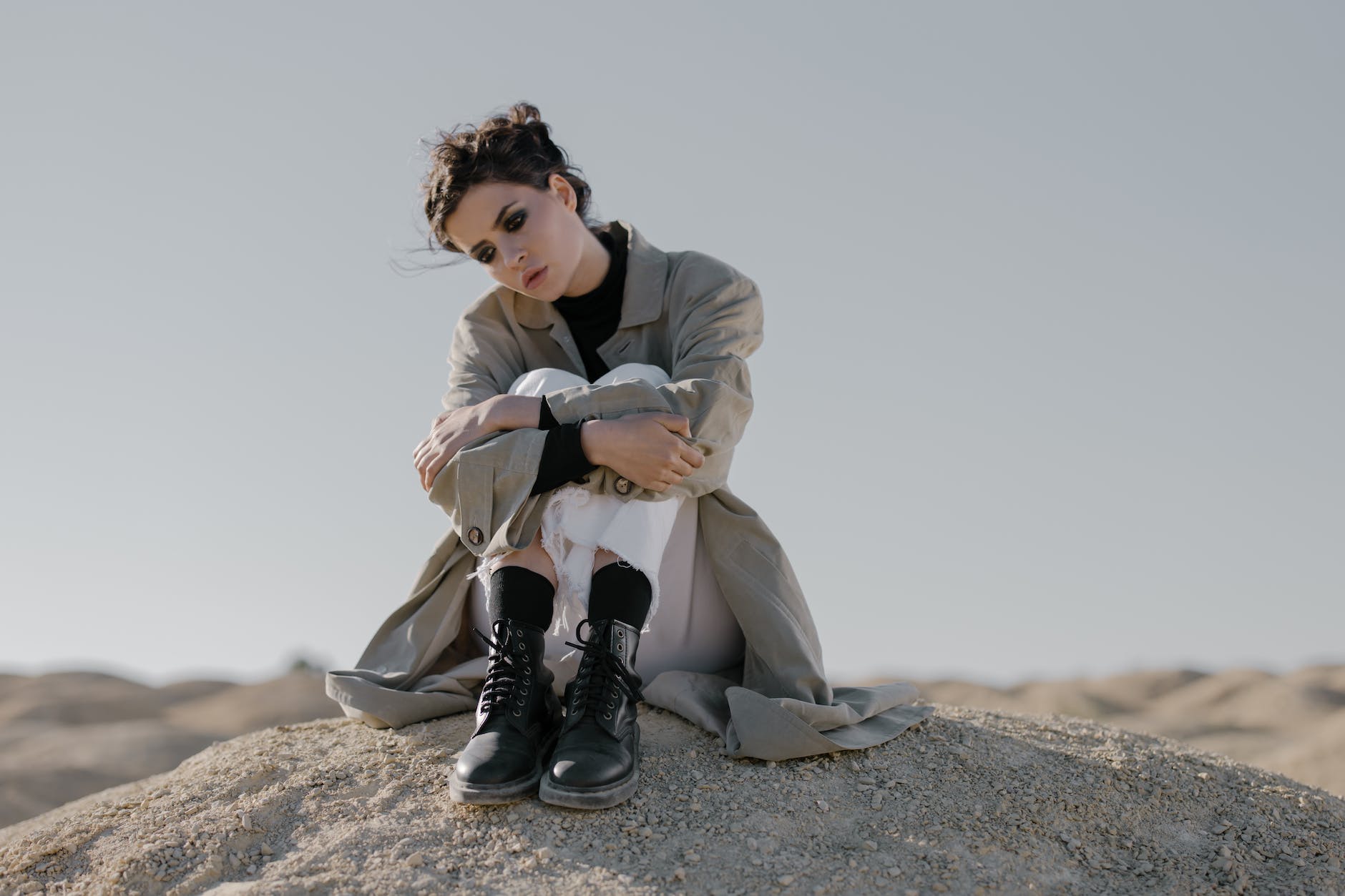 woman in a trench coat and black boots sitting on dirt ground - Ethical Isn't Always Best