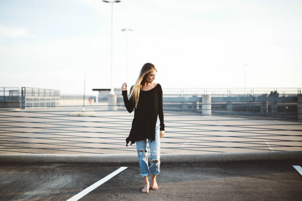 woman stands barefoot on top of parking garage wearing jeans - What Is Fair Trade