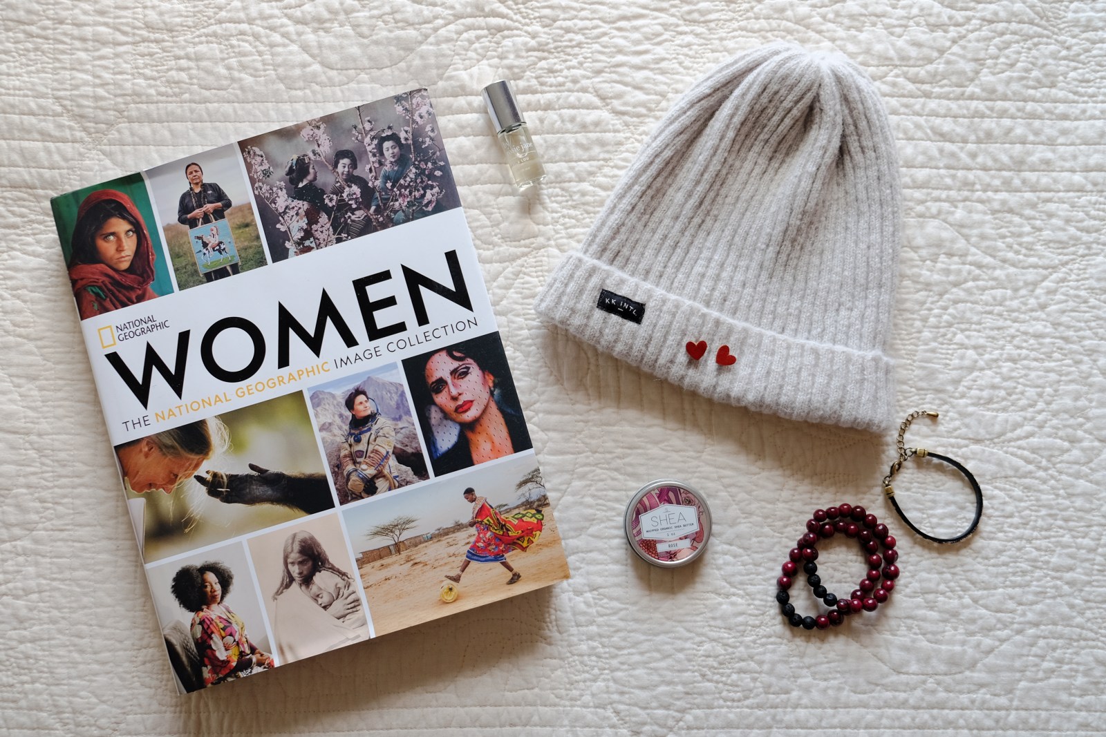 ethical blogger press coverage media kit - coffee table book with hat, bracelets, lotion, and perfume on white quilt