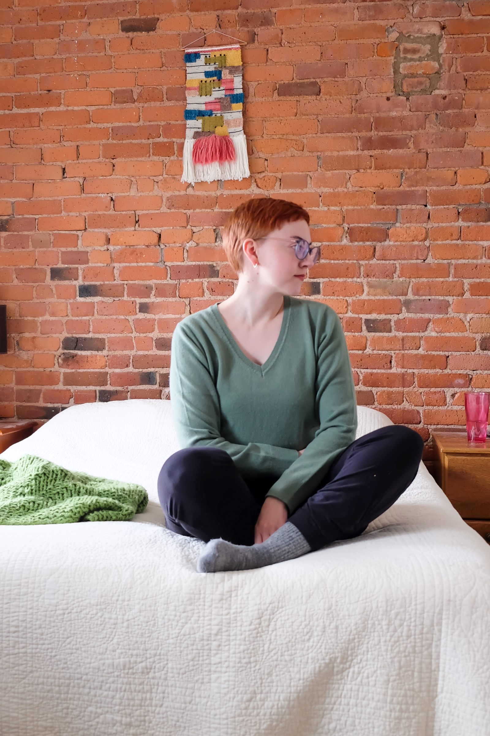 pixie cut using clippers - Leah sits on bed with white quilt wearing green sweater