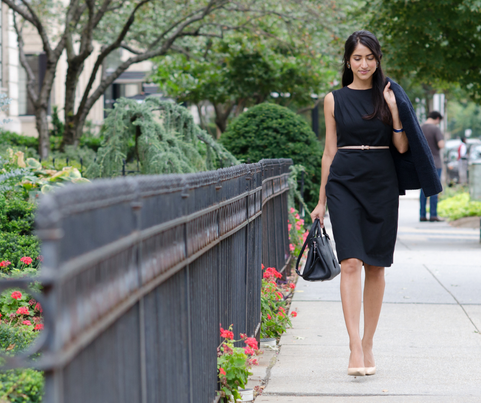 woman strolls on sidewalk wearing a black shift dress with neutral pumps - Maven Women Professional, Ethical Dresses