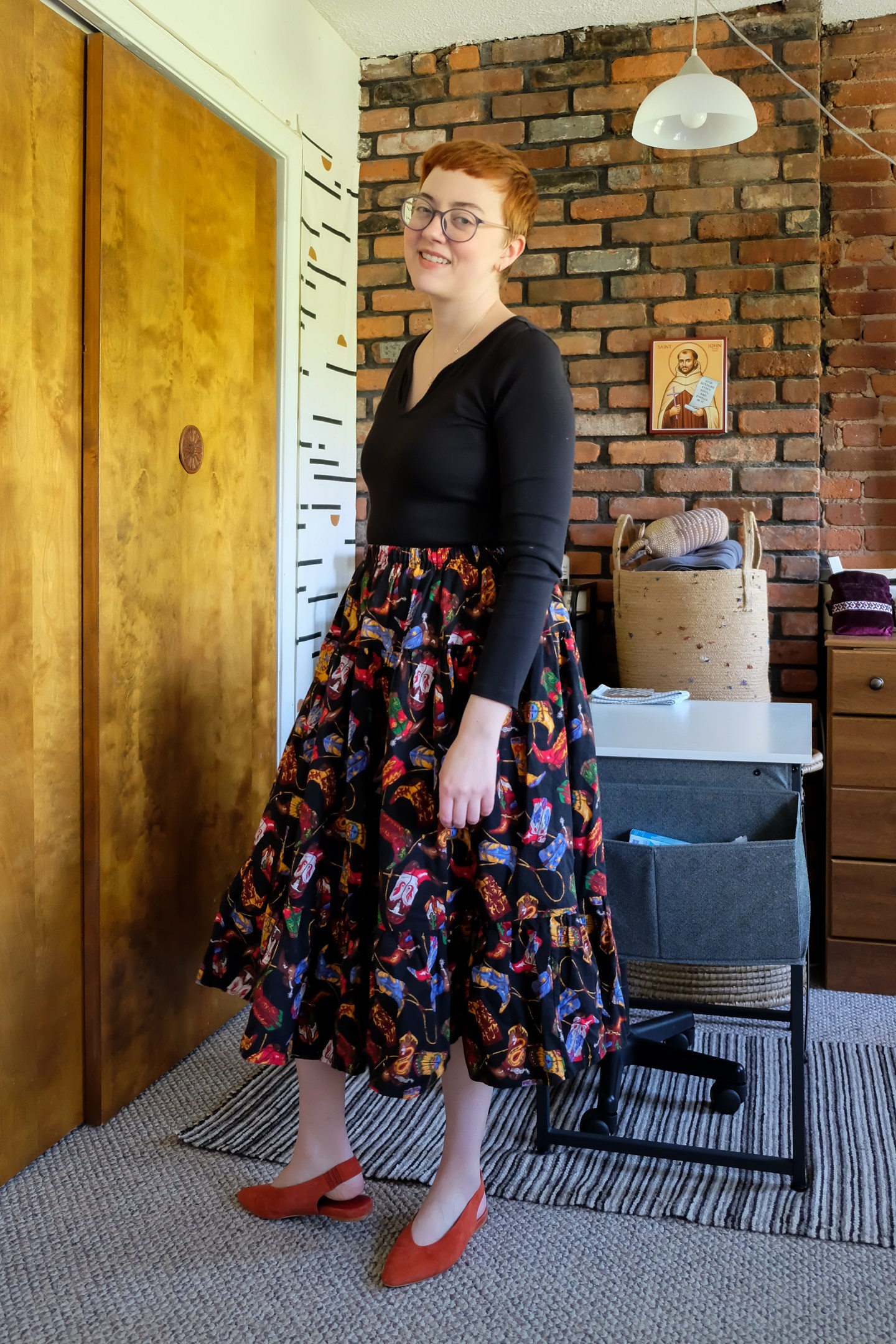 Leah wears a black top with a black circle skirt with colorful cowboy boot print, and red shoes - Big News and a Big Skirt