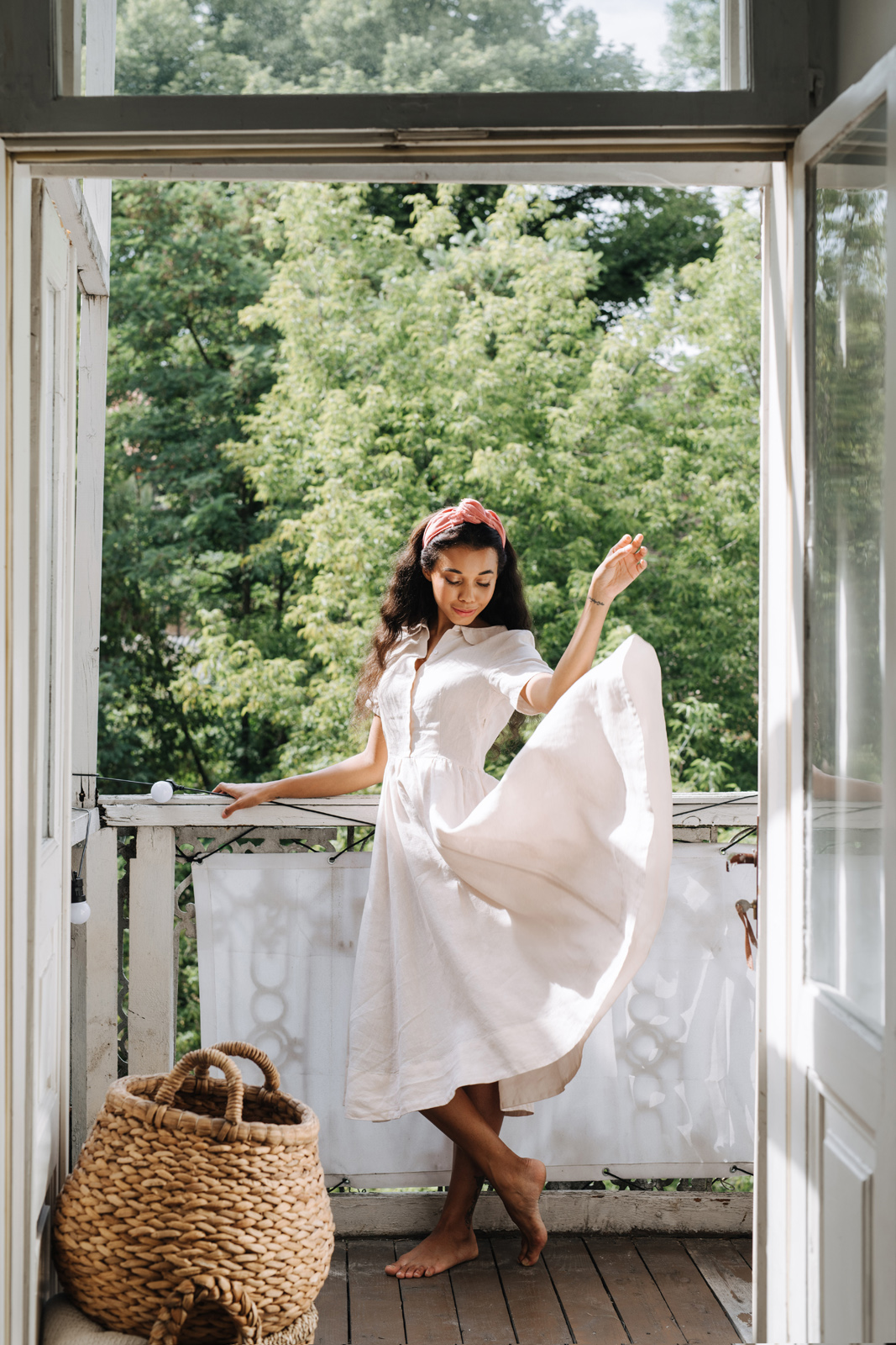a woman stands on a porch wearing a white linen dress - Sustainable Linen Clothing Brands