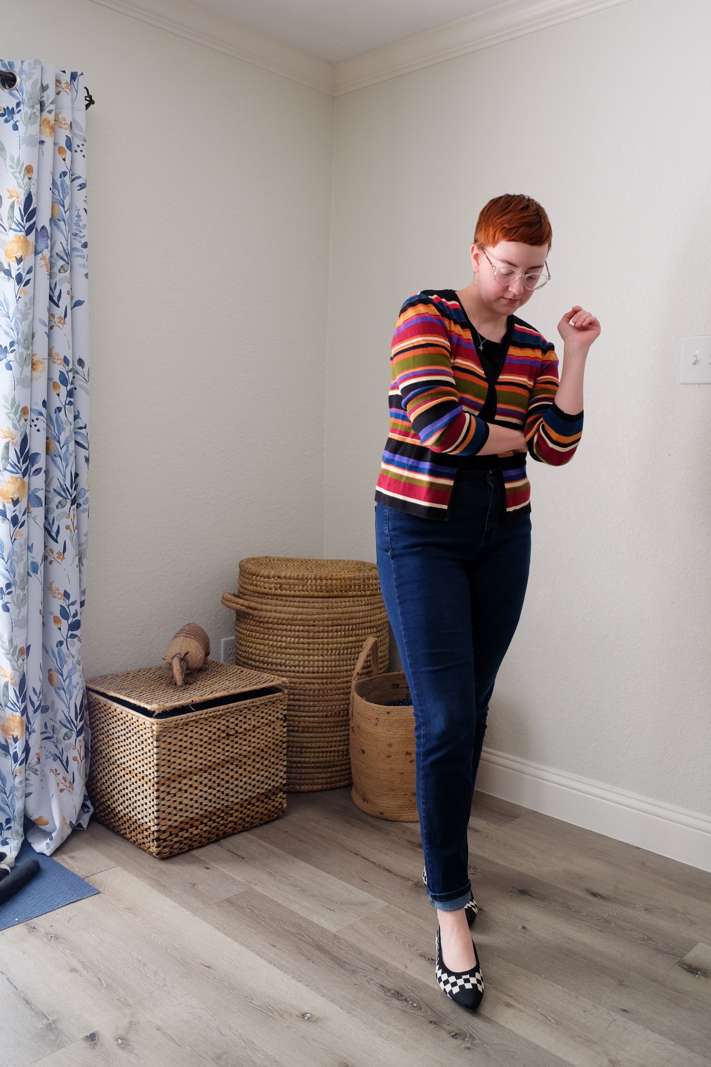 Leah stands in her bedroom wearing a colorful striped cardigan, jeans, and checkered flats - Vivaia Knit Flats Review