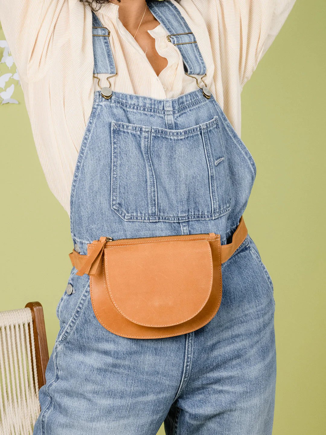 torso shot of person wearing overalls and cognac leather belt bag with lime green wall behind them - ABLE Sale 2022 Picks
