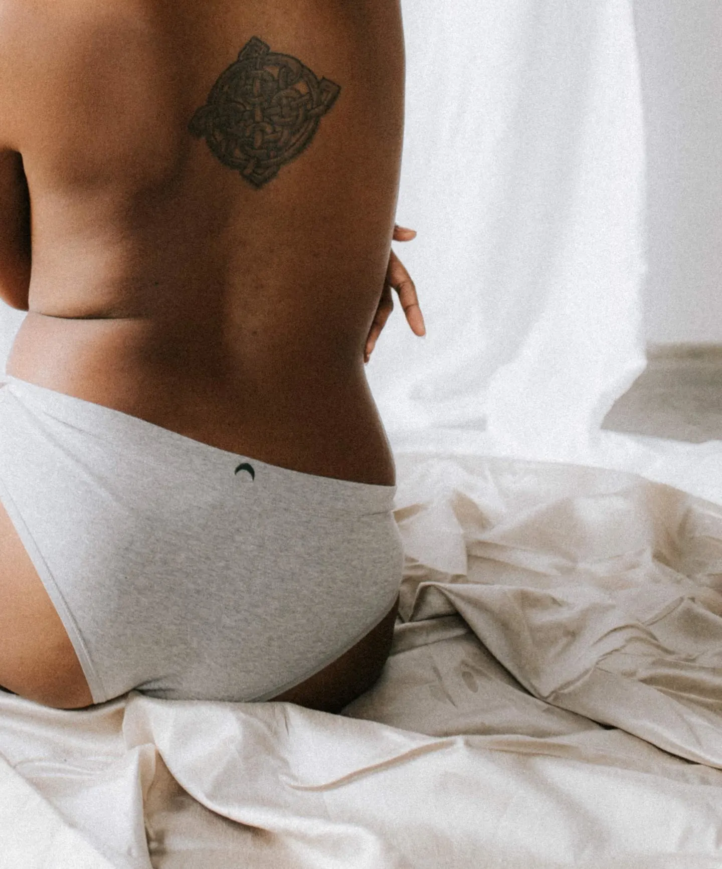 woman with medium caramel skin and back tattoo sits in gray underwear - PFAS in Thinx lawsuit