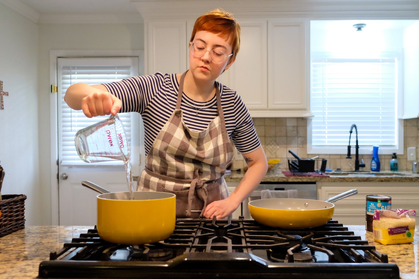 image shows Leah pouring water from glass pyrex into a yellow pot on a stove