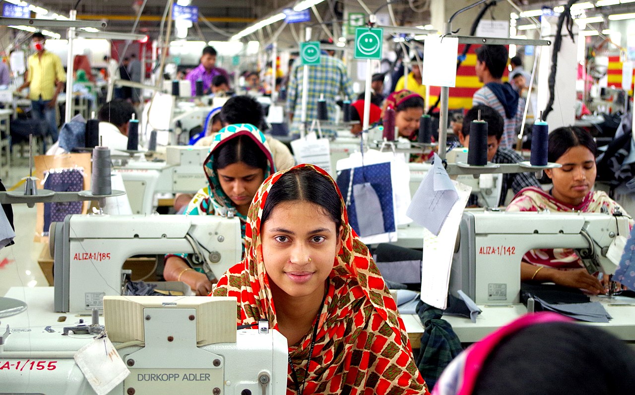 young women in colorful head scarves sit behind sewing machines in a Bangladesh garment factory - ten years rana plaza